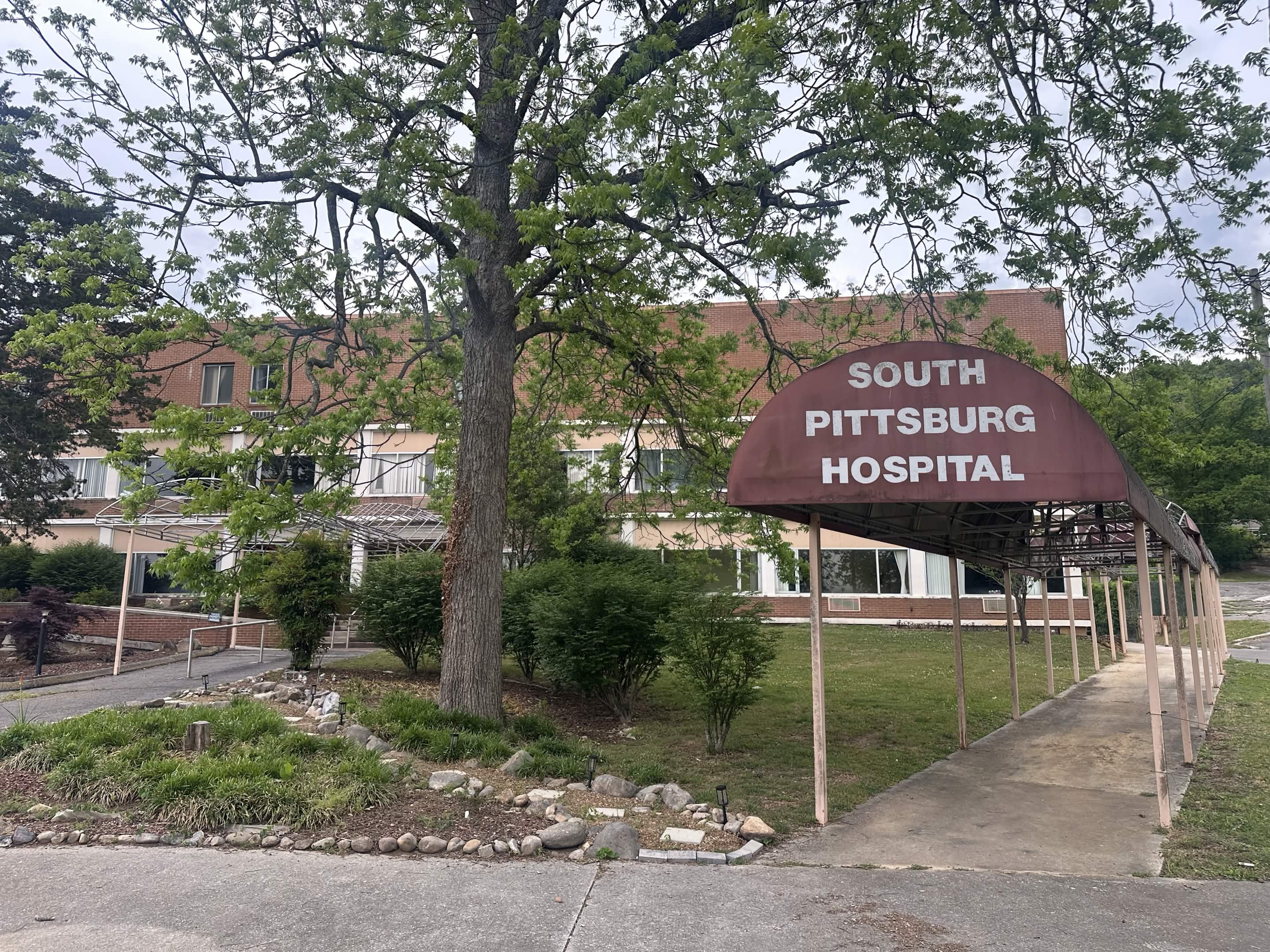 The front of the Old South Pittsburg Hospital, a low brick building with a long covered walkway running to a brown awning lettered SOUTH PITTSBURG HOSPITAL